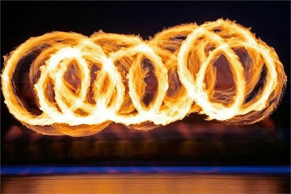 Long-exposure photo of a fire performance, with rings of flame traced against the night sky